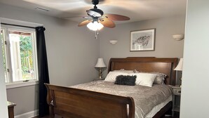 A bedroom with a wooden bed, a ceiling fan, a window with curtains, a rug, and a framed picture on the wall. - Crystal Conch sleeps 16, private home close to beach access (Emerald Isle)