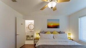 A bedroom with a bed, bedside lamps, a ceiling fan, a painting, and a bathroom with a mirror and sink. - Family Friendly & King Suite & Fire Pit, 9 Mil DT (Austin)