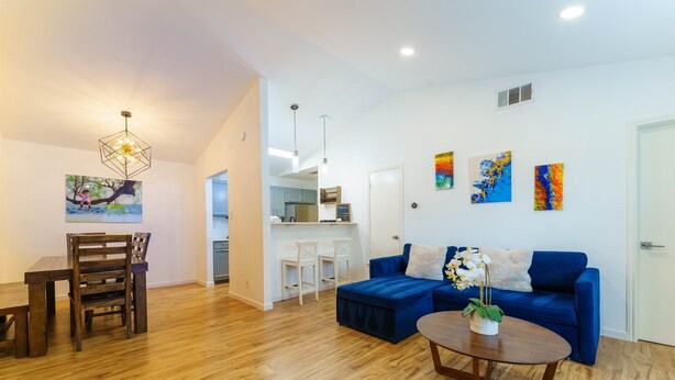 A modern living room with a blue sofa, wooden dining table, and chairs. There is a kitchen area visible in the background. - Family Friendly & King Suite & Fire Pit, 9 Mil DT (Austin)