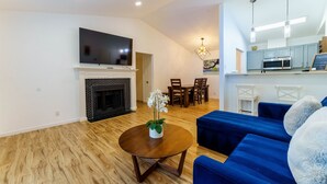 A modern living room with a fireplace, a flat-screen TV, a dining area, and a kitchen with a microwave. - Family Friendly & King Suite & Fire Pit, 9 Mil DT (Austin)