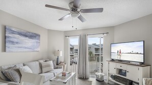 A modern living room with a sofa, coffee table, TV, and a ceiling fan. - Live Like a Local Too (Miramar Beach)