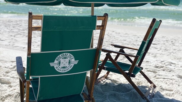 A beach chair with a green umbrella and a logo on the backrest. - Live Like a Local Too (Miramar Beach)