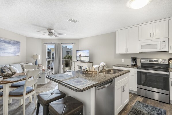 A modern kitchen with white cabinets, a stainless steel oven, and a granite countertop. - Live Like a Local Too (Miramar Beach)