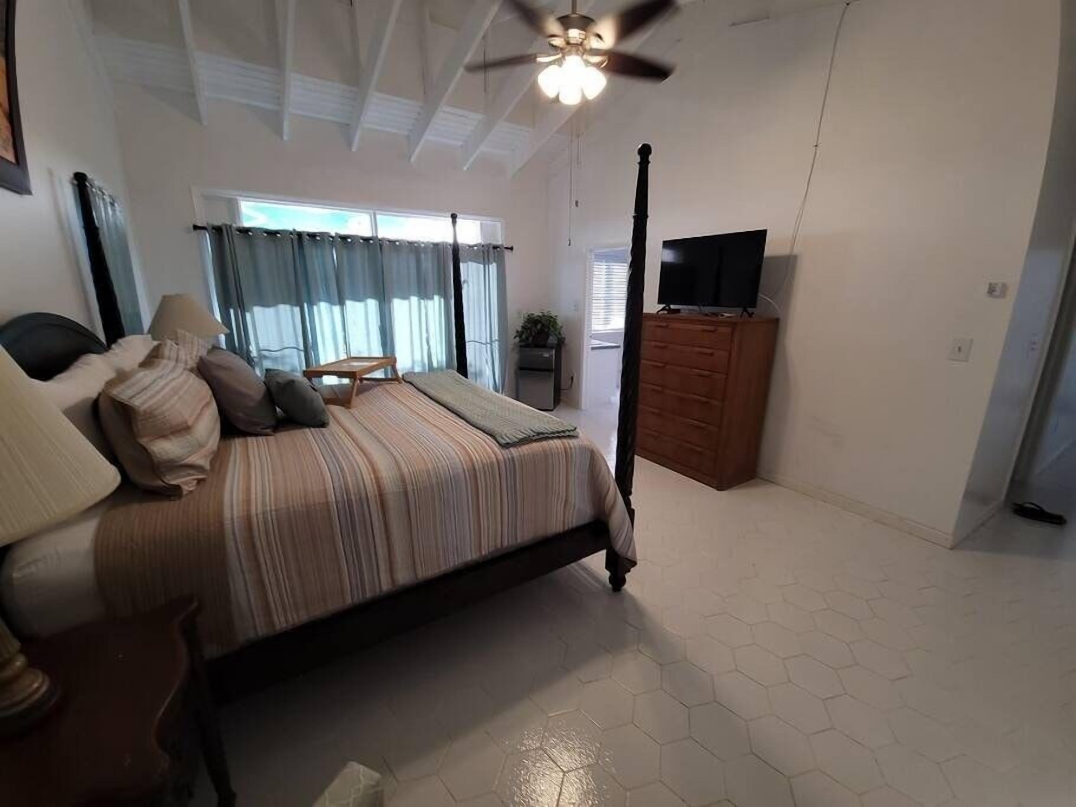 Ein Schlafzimmer mit einem Himmelbett, einem Deckenventilator, einer hölzernen Kommode und einem Fernseher auf einem Schrank.