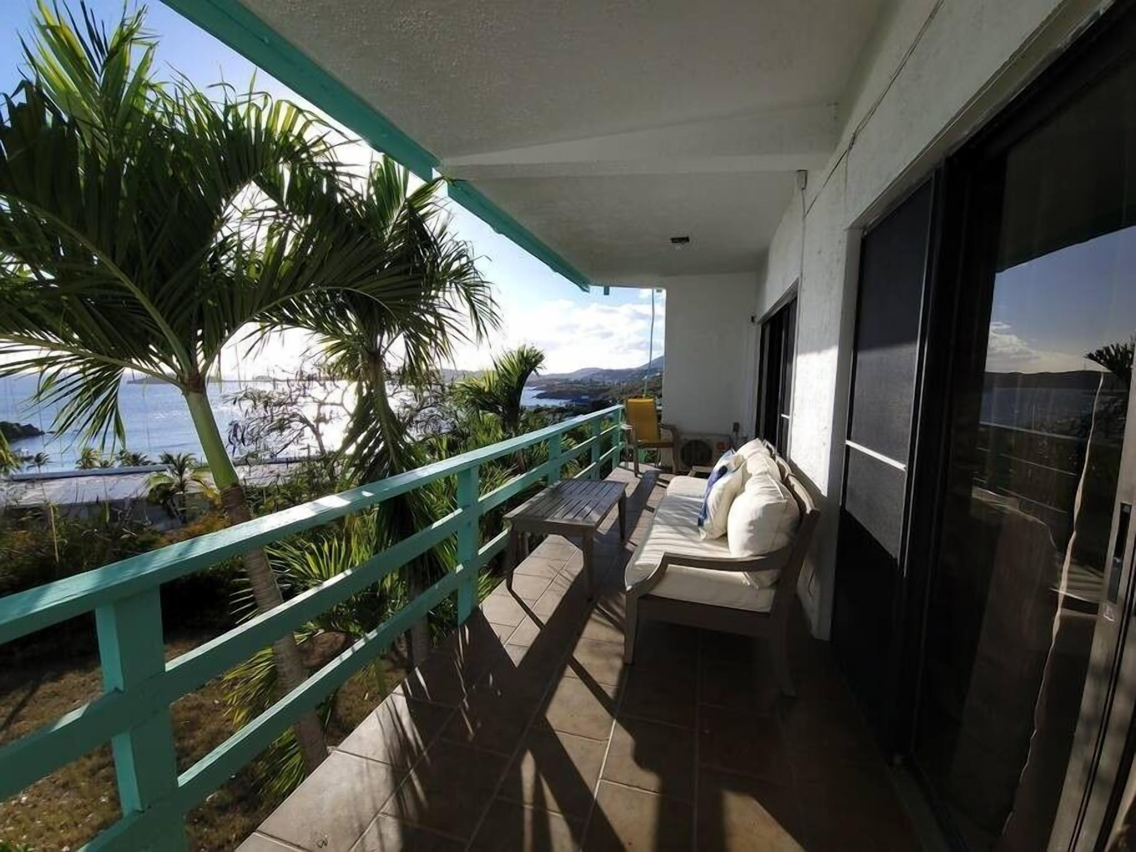 A balcony with a white sofa, a small table, and a view of the sea and mountains.