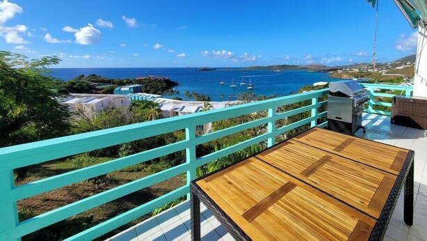 Un balcon avec vue sur l’océan, une table en bois et une rambarde turquoise.
