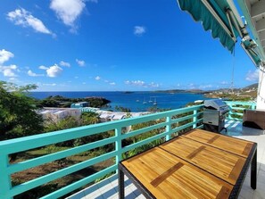 En balkon med havudsigt, et træbord og et turkis gelænder.