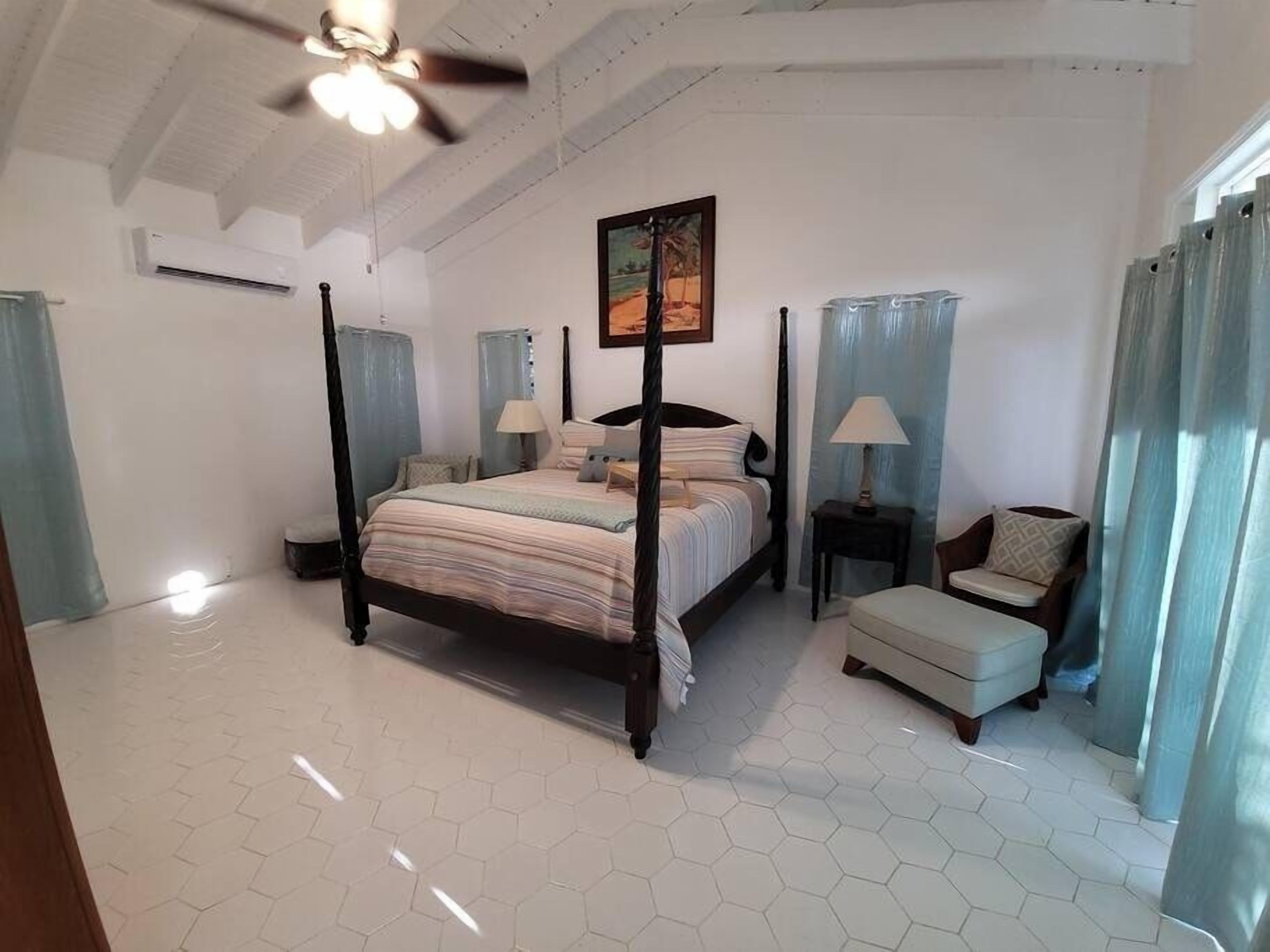 A bedroom with a four-poster bed, a ceiling fan, a painting on the wall, and a window with curtains.