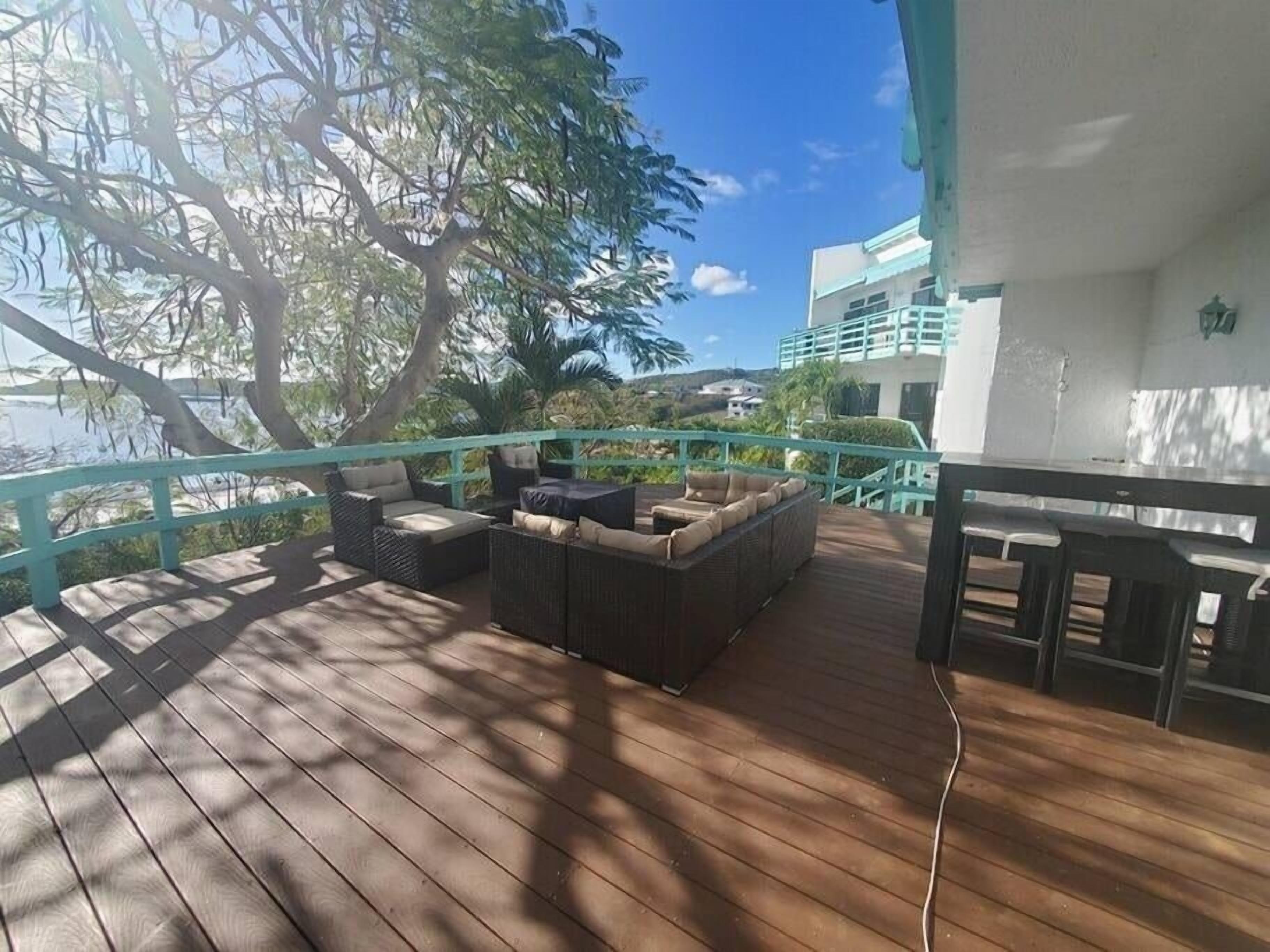 A wooden deck with outdoor furniture, a railing, and a view of a building and trees.