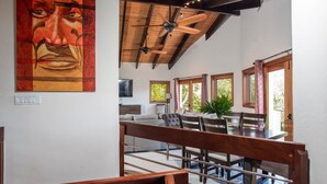 Un vaste espace dédié à la salle à manger, avec une table et des chaises en bois, un ventilateur de plafond et de grandes fenêtres qui laissent entrer la lumière naturelle.