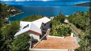 Une propriété située sur la côte, avec une grande maison dotée d’un toit en pente, entourée d’une végétation luxuriante et offrant une vue sur l’océan.