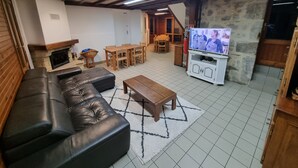 Tunnelmallinen olohuone, jossa on musta nahkasohva, puinen sohvapöytä ja valkoisessa kaapissa oleva televisio. Huoneessa on kiviseinä ja katossa puiset palkit.