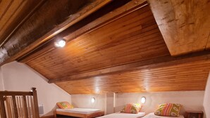 Tunnelmallinen ullakkohuone, jossa on puulattiat ja kaltevat katot. Huoneessa on kaksi erillistä sänkyä, värikkäitä tyynyjä ja yöpöydällä seisovat lamput.