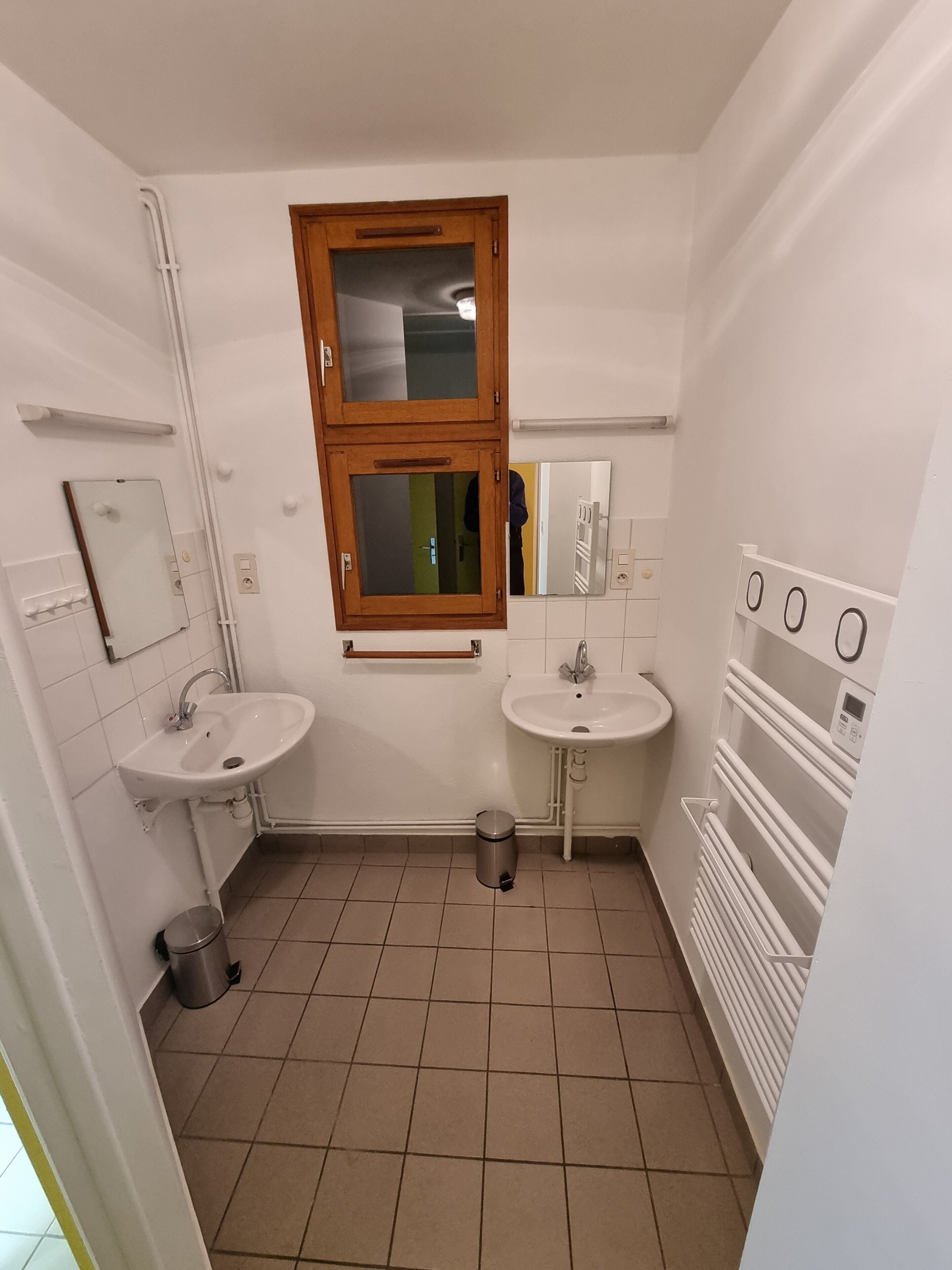Une petite salle de bain propre, équipée de deux lavabos, d’un miroir, d’une fenêtre et d’un radiateur.