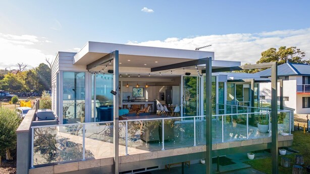 Una casa moderna con balcón acristalado, espacio de cocina visible y vista despejada del paisaje circundante.