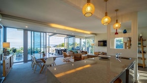 Una cocina moderna con una isla grande, un área de comedor con sillas y una mesa, y un salón con sofás y una televisión.