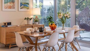 Un comedor moderno con una mesa de madera, sillas blancas y vistas al exterior a través de amplios ventanales.