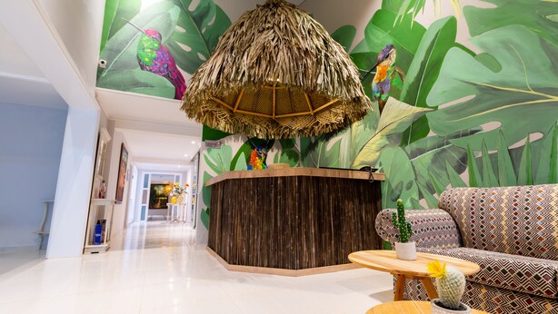 A reception area with a wooden reception desk, a hanging woven light fixture, a patterned sofa, and a small table with a potted plant. - Casa Chunuu hotel boutique (Santa Marta)