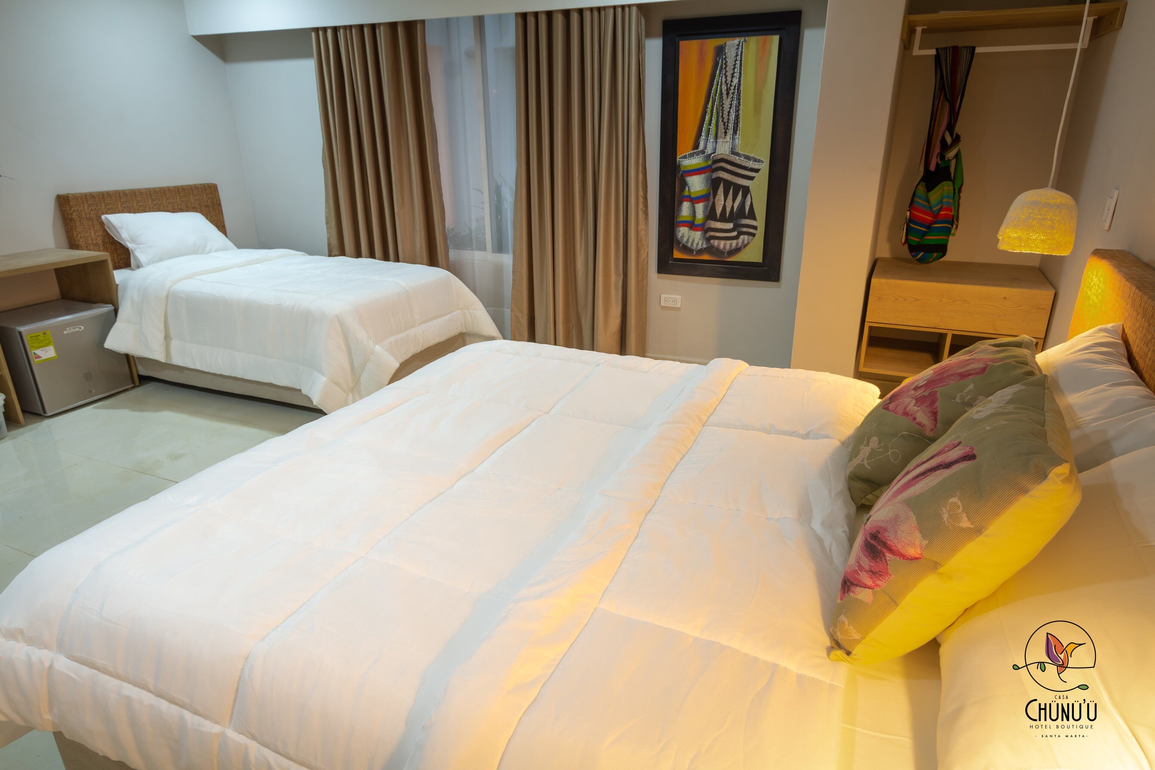 Una habitación de hotel con dos camas, un cabecero de madera, una mesita de noche, una lámpara y un cuadro en la pared.