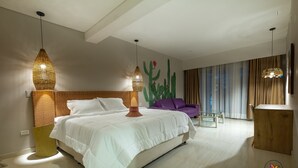 A modern hotel room with a large bed, two pendant lights, a cactus wall art, a purple sofa, and a wooden side table. - Casa Chunuu hotel boutique (Santa Marta)
