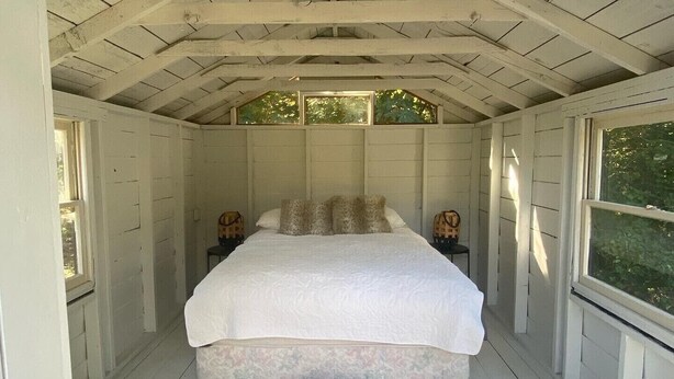 A bedroom with a large bed, wooden beams, and a view of greenery outside. - Wedding/Event 7 acre MCM Main house, 4 cabins, Bunkhouse IG astroranchpdx (Happy Valley)