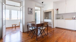 Une cuisine moderne avec des meubles blancs, une table à manger en bois et un petit tabouret.