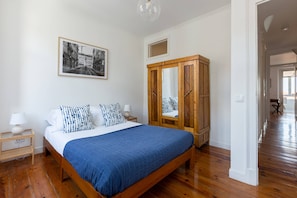 Un dormitorio con cama, armario de madera, mesitas de noche, un cuadro enmarcado y un pasillo.
