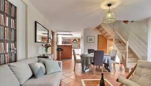 A living room with a sofa, dining table, and chairs. There is a staircase leading to another level.