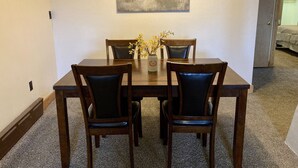 Uma sala de jantar com uma mesa e quatro cadeiras, um vaso com flores e um quadro na parede.
