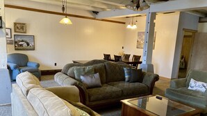 Uma sala de estar com sofá seccional, um sofázinho, uma mesa de centro de vidro e um espaço de jantar com mesa e cadeiras.