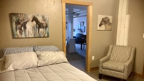Quarto com cama grande, poltrona estampada e duas pinturas com tema de cavalos nas paredes.