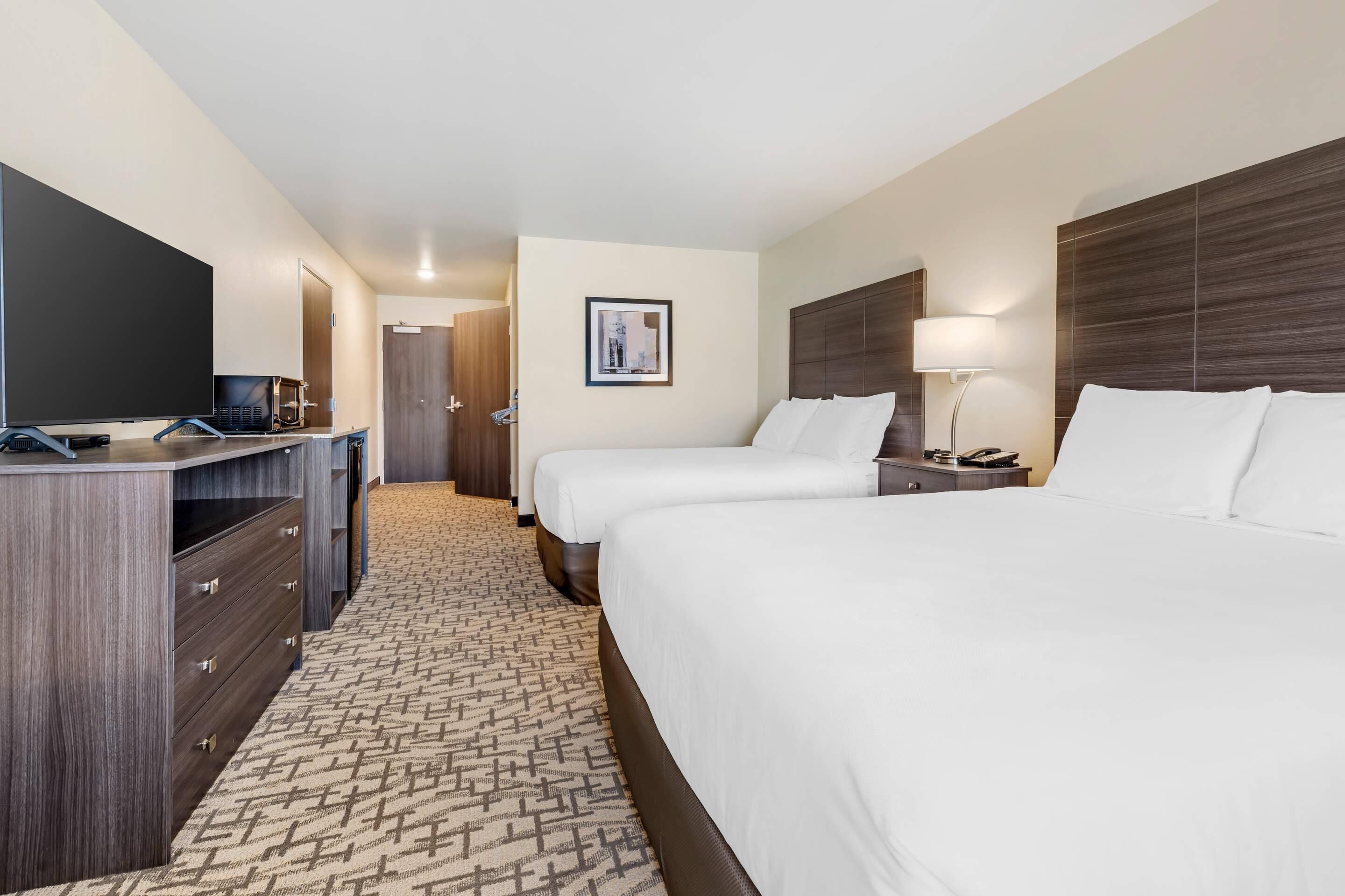 A hotel room with two beds, a TV, a desk, and a carpeted floor.