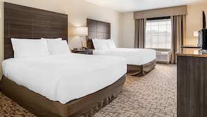 Quarto de hotel com duas camas, uma escrivaninha, uma luminária e uma janela grande com cortinas.