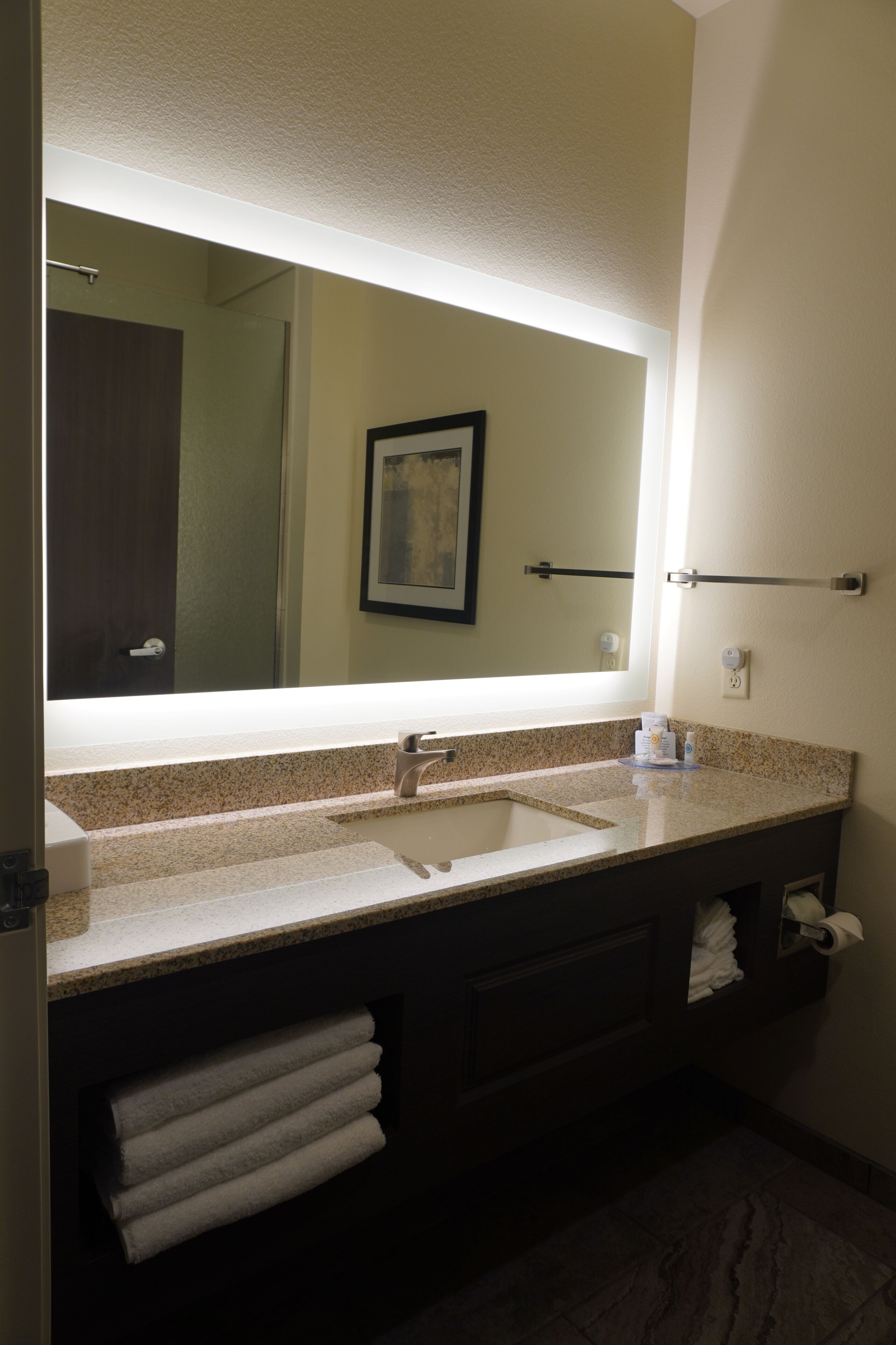 A bathroom with a large mirror, a sink, and a towel rack.