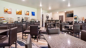 Uma área de refeições de hotel com várias mesas e cadeiras, um buffet e uma cozinha.