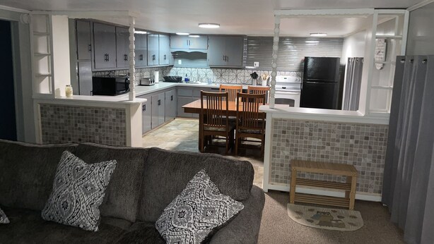 Una cocina moderna con armarios grises, una zona de comedor con sillas de madera y un sofá gris con cojines estampados.