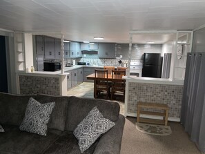 A modern kitchen with grey cabinets, a dining area with wooden chairs, and a grey sofa with patterned cushions. - Piedmont Lake Marina Road Cabin Rental (Freeport)