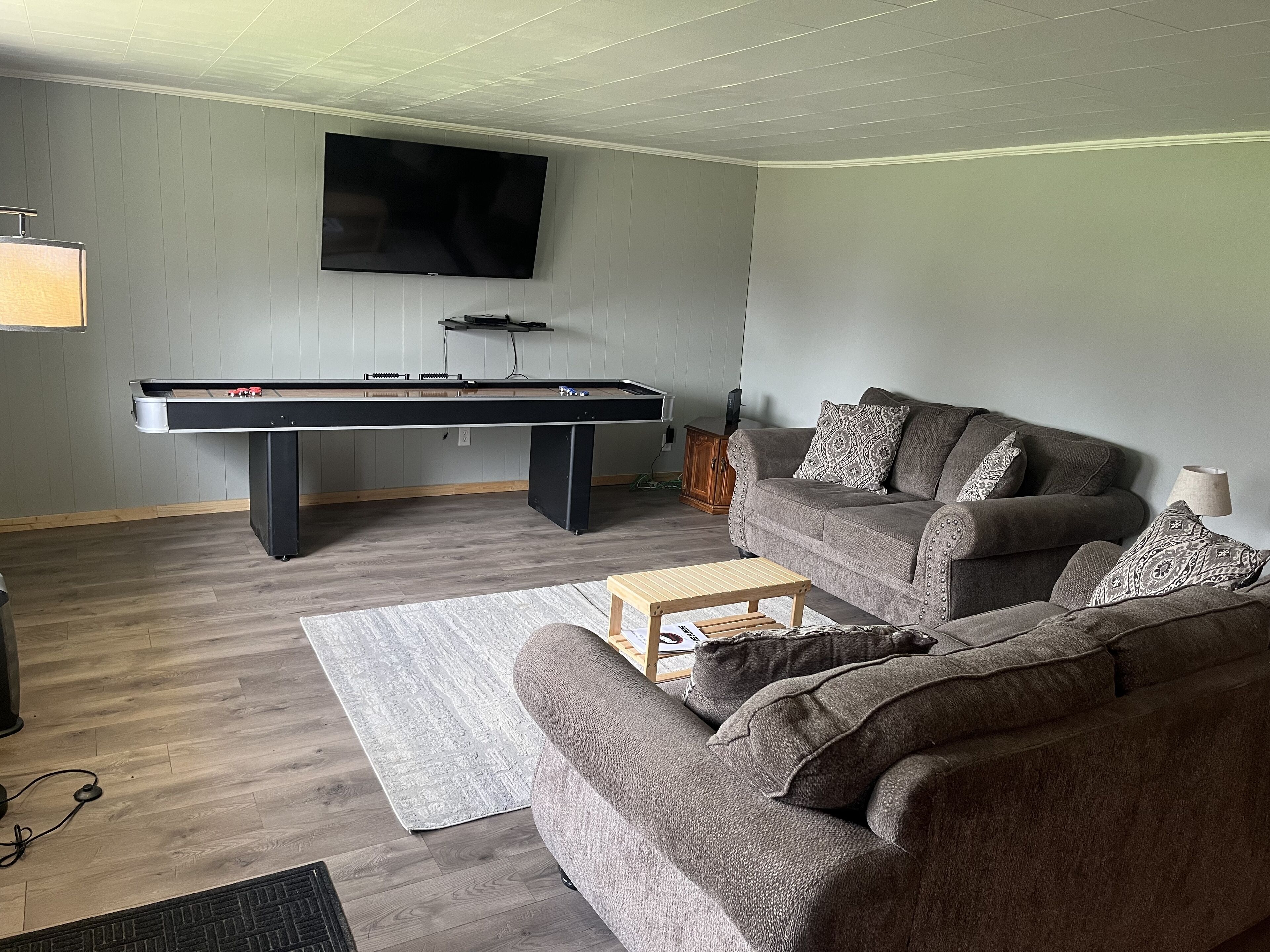 Een woonkamer met een pooltafel, een bank en een aan de muur bevestigde televisie.