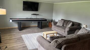 Een woonkamer met een pooltafel, een bank en een aan de muur bevestigde televisie.