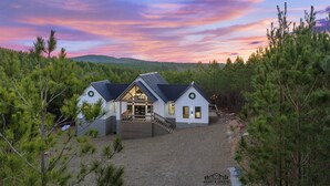 Una casa moderna de dos pisos con un porche cubierto y vistas al bosque circundante.