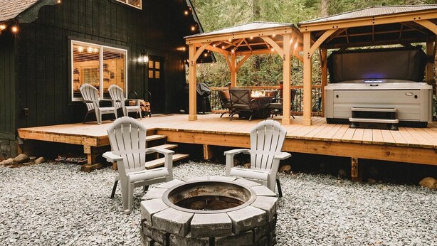 A cabin with a deck, outdoor seating, a fire pit, and a grill area.