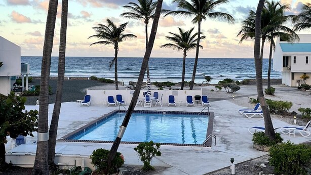 Uma área de piscina com espreguiçadeiras, palmeiras e vista para o oceano.
