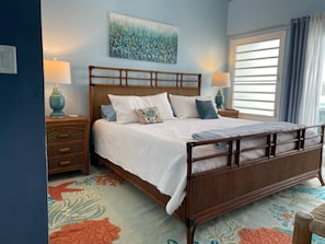 A bedroom with a wooden bed, a nightstand, a lamp, a painting on the wall, and a window with curtains.