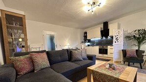 A modern living room with a dark grey sofa, a wooden coffee table, and a kitchen area in the background.