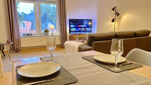 A dining area with a table set for two, a television in the background, and a sofa in the living room.