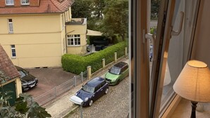 A room with a view of a lake, a yellow building, and parked cars.