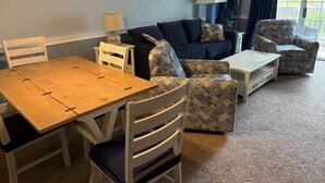 Una sala de estar acogedora con una mesa de comedor de madera, dos sillones estampados, un sofá y una lámpara.