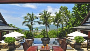 A patio with a table and chairs, surrounded by potted plants and umbrellas, overlooking a scenic view with palm trees and a distant landscape. - Nakawanna Villa (Kamala)