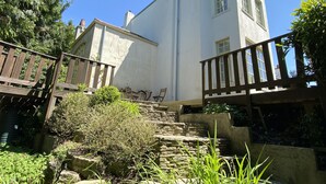 A two-story building with a stone staircase leading to a wooden deck. - Large beautiful unusual house with lots of character and art on the walls. (Bournemouth)
