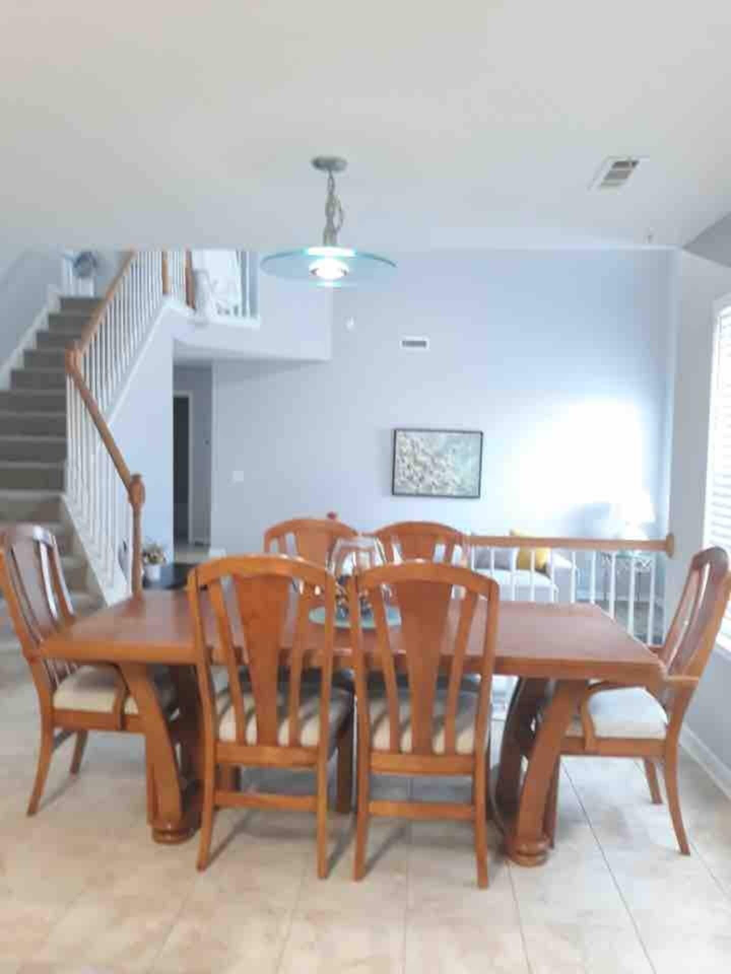Un espace repas avec une table et des chaises en bois, un escalier et un luminaire au plafond.